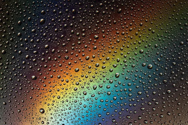 Drops of water on the glass in the light of the rainbow. Abstraction. Background.