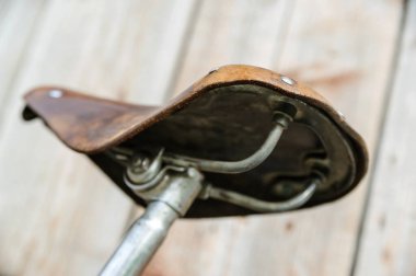 Deri bir bisiklet eyeri. Ahşap bir arka planda eski bir eyer. Alt görünüm.