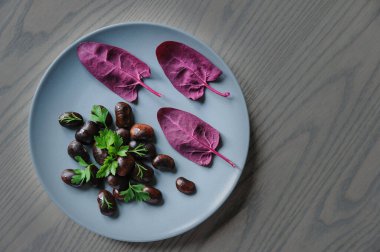 Koyu fasulye ve kırmızı ıspanak yapraklı tabağı ahşap masanın üstüne koyun..