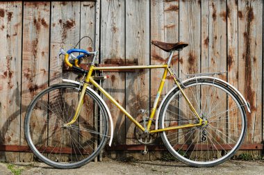 Tahta bir kapının arkasında eski bir bisiklet. Eski kapının önüne park edilmiş eski bir bisiklet..