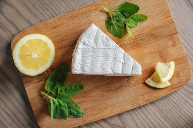Kesme tahtasının üzerinde Brie peyniri, limon ve ıspanak var..