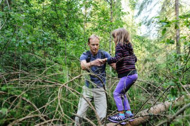 Ormanda yürürken engelleri aşmak. Yetişkin, kızın devrilmiş ağacı geçmesine yardım ediyor..