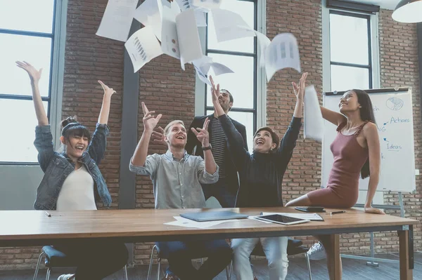 Mutlu çok ırklı grubunu belgeleri atma ve oturma ve çalışma, ayakta iken mutlu görünüyordu genç iş adamları modern ofiste yerleştirir. Başarı kutluyor. Kazananlar zaferi heyecanlı