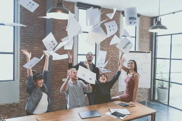 Başarı kutluyor. Belgeleri atma ve oturma ve çalışma, ayakta iken mutlu görünüyordu genç iş adamları çok ırklı grup modern ofiste yerleştirir. Kazananlar zaferi heyecanlı