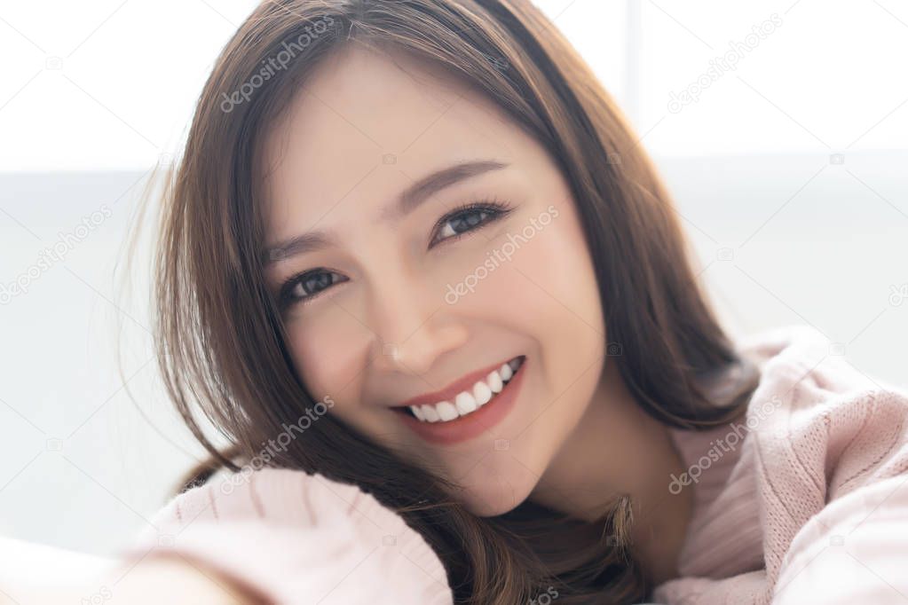 Closeup portrait of inspired caucasian Asian lady wearing knitted sweater pink cold smilling and taking selfie at her home.Concept woman lifestyle and winter. Model fashion shooting. Autumn, winter season.