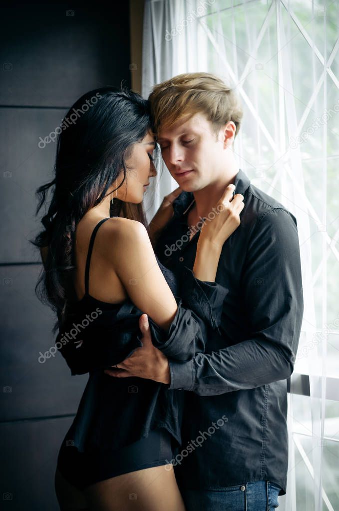 Handsome young man and sexy young woman in black lingerie are hugging in room,so tender, romantic, tempting, sensual.