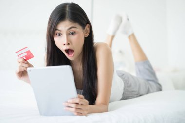 Tablet kullanma ve kredi kartı onu görmek büyük satış duyuru Web sitesinde sörf internet bir onu bir yatakta yatarken süre tutarak hayran Asyalı kadın oda. Alışveriş online, şok erkek beklenmeyen e-posta veya ileti alma
