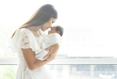 Genç Asya Anne öpüşme yeni doğan bebek kolunda onu pencere, annelik kavramı, yumuşak görüntü güzel aile, Anne gün kavramı.