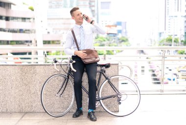 Şehir ayakta telefon kullanarak, bisikletiyle, gülümseyen ve uzağa bakarak kendine güvenen genç işadamı.