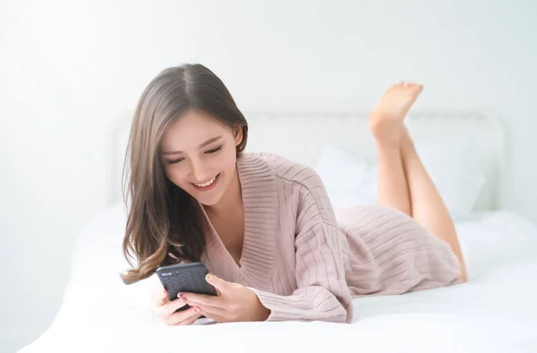 아시아 여자를 분홍색 스웨터 차가운 침대에 휴대폰 스마트폰에 인터넷 라이프 — 스톡 사진