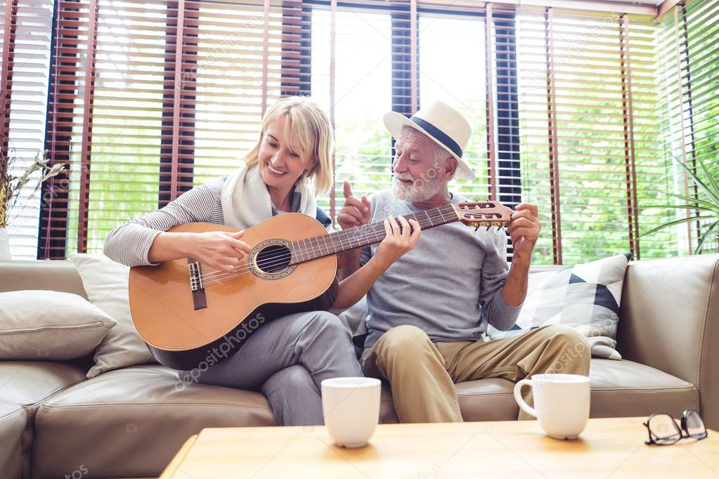 Loving mature couple sitting on the sofa while wife plays the guitar, sings the songs together in living room