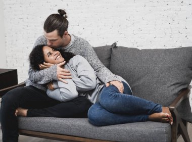 Tatlı çift evde oturma odasında kanepede uzanmış iken kazak ve cuddleling giyiyor. Gerçek sevgi ve hassasiyet