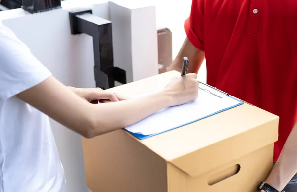 Close-up of a Asian woman appending signature sign on clipboard after accepting receive boxes from delivery man, woman sign on the box, receive delivery concept.