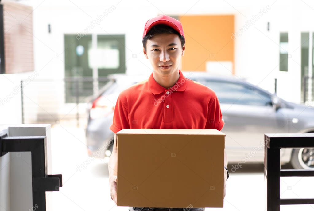 Happy delivery person in red uniform holding cardboard box standing in front the home customers,Delivery and  Service concept, Packing Concept.