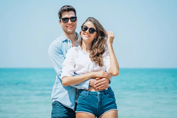 Portrait of sweet couple embracing and having fun on coast behind blue sky