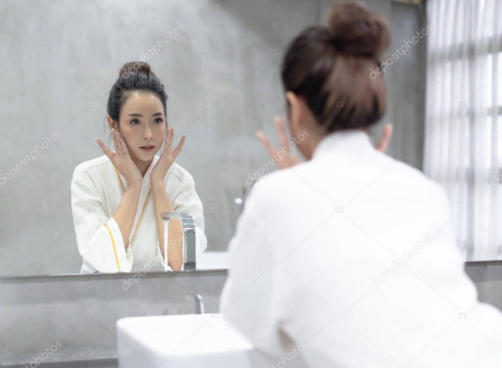 Facial Beauty.Young beautiful Asian woman applying moisturizer c