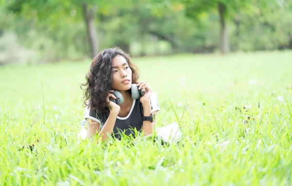 Hermosa mujer asiática joven acostada en la hierba con auriculares y l — Foto de Stock