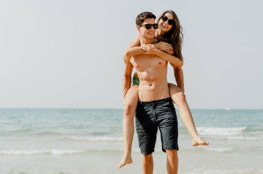 Gülümseyen kız arkadaşını sırtında taşıyarak gülen genç bir çift.