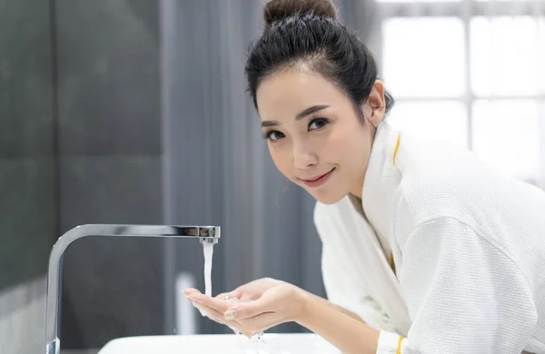 Hermosa chica asiática en albornoz lavándose la cara con agua abo —  Fotos de Stock