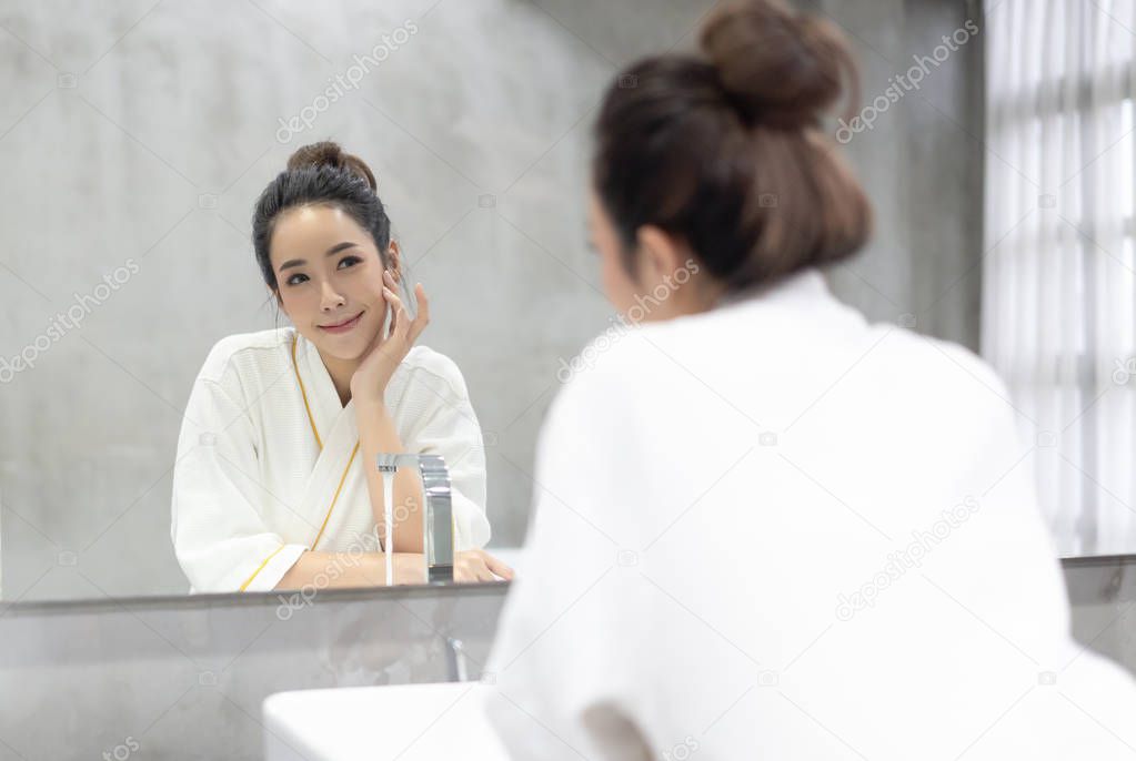 Facial Beauty.Beautiful smiling young Asian woman in bathrobe ap