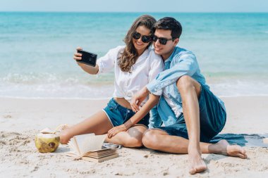 Güneş gözlüğü içinde romantik çift selfi alarak sahilde oturan