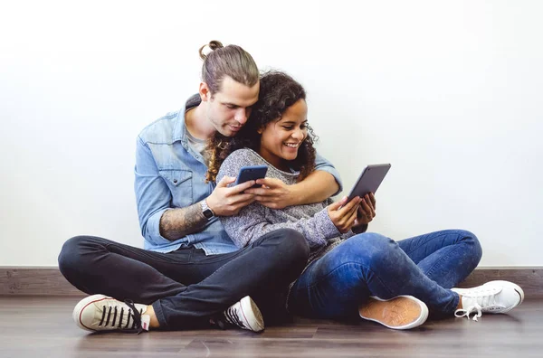 Retrato de una joven pareja multiétnica sentada en el suelo usando — Foto de Stock