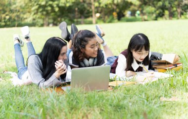 Yeşil çim okuma kitapları üzerinde yatan mutlu çok ırklı arkadaşlar ve 
