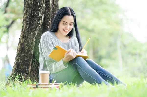 Étudiante souriante assise dans un parc. Collège fille prendre note — Photo