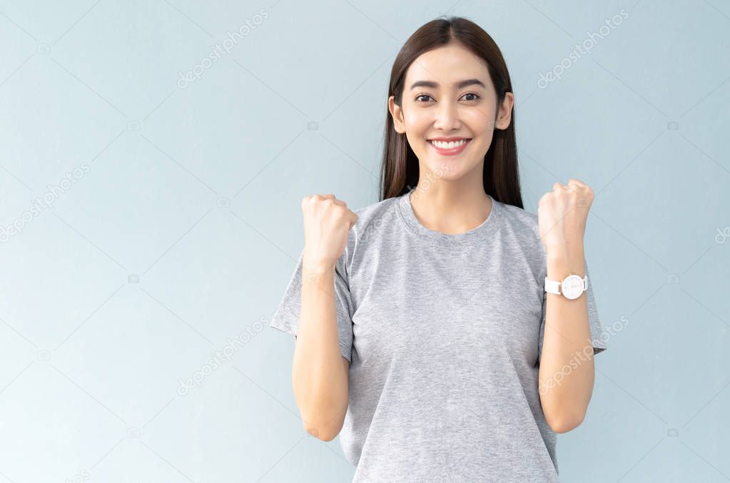 Happy young Asian girl celebrating her success, keeps hands clen