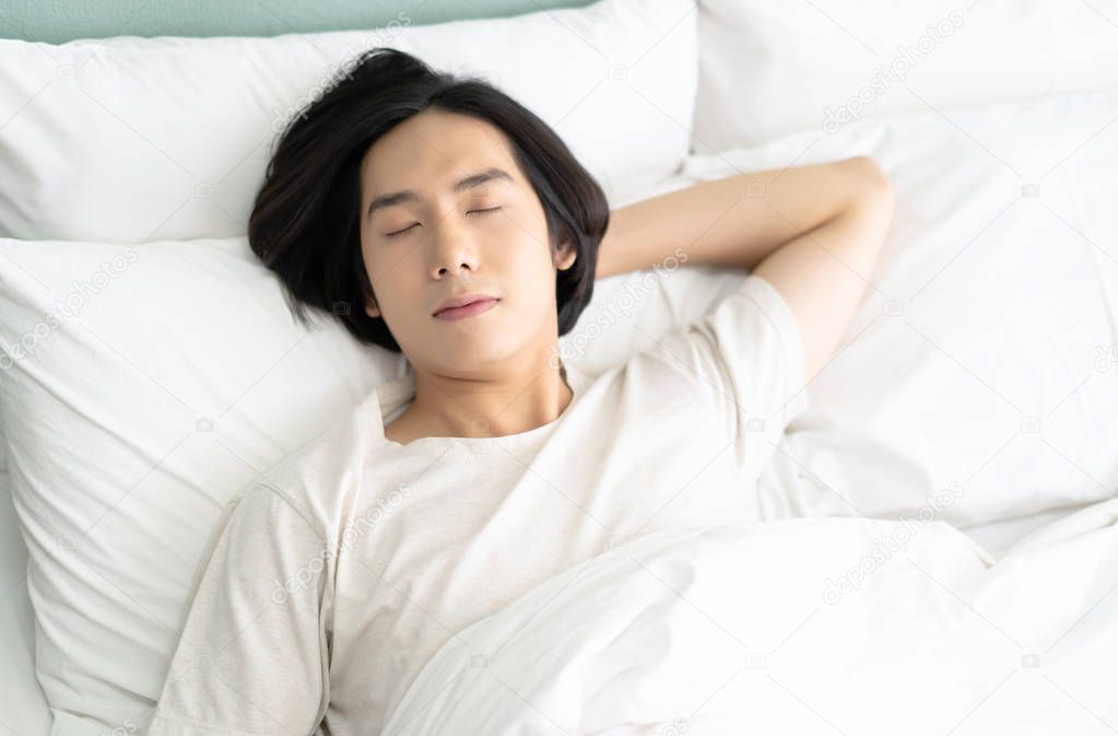 Attractive young Asian man is sleeping in his bed. He is lying in his bed with relaxation. Guy enjoying sweet dreams and enough rest concept