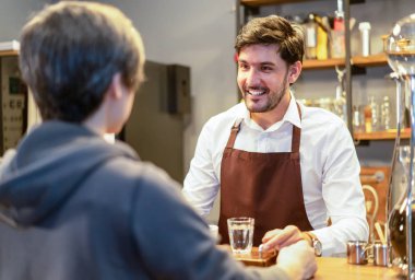 Konte arkasında duran gülümseyen çekici sakallı barista garson