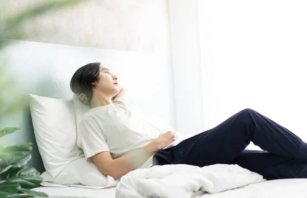 Seitenansicht eines jungen asiatischen Mannes, der in seinem Bett liegt und sich im Bett entspannt. — Stockfoto
