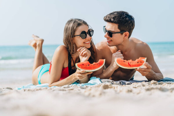 Happy young couple holding and eating slices of watermelon on th