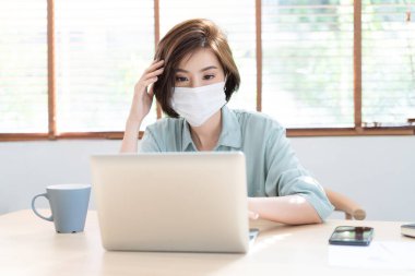 Korunma gribi ve covid-19 için koruyucu maske takan Asyalı genç iş kadınının portresi. Kendini izole etme ve karantina sürecinde bilgisayarın başında çalışıyor. Evden çalışma kavramı.