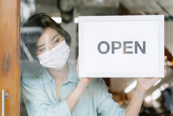 Portrait of young Asian woman owner with face mask standing at restaurant and ready for the situation and reopen shop after lockdown due to outbreak of coronavirus covid-19. Small Business Owner.