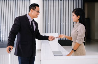 Genç Asyalı yakışıklı işadamı otel kontrolüne resepsiyondaki kadınla birlikte gelir. İş seyahati konsepti..