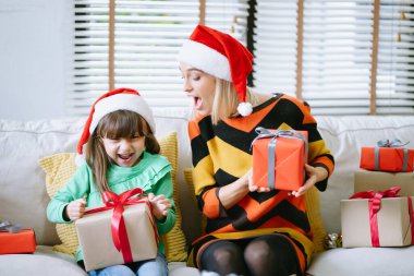 Noel Baba şapkalı anne ve kız Noel hediyelerini kahkaha ve heyecanla paylaşıyorlar. Sıcak tatil anı, sevgi, neşe ve şenlikli aile kutlamalarının büyüsünü yansıtır..