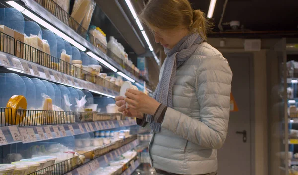 Süpermarkette süt ürünlerini seçen güzel bir genç kadın. Kavanoz robiola, küflü mavi peynir, Belçika peyniri, brie defamilier...