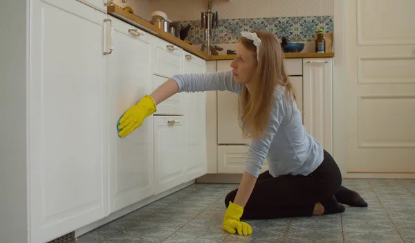 Tired young pretty woman in protective yellow gloves cleaning kitchen. She slowly washing a kitchen cabinets. Domestic daily life, housekeeping.