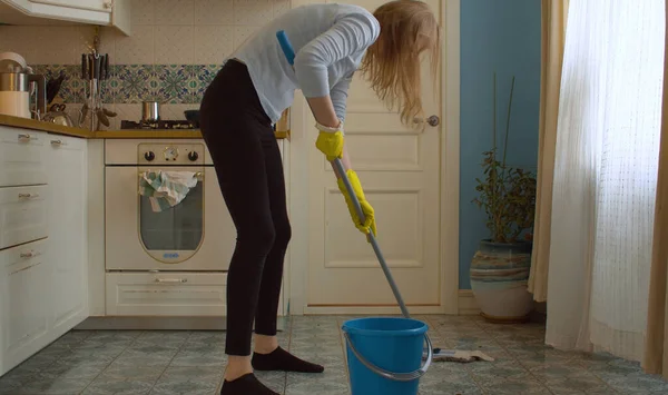 穿着黄色防护手套的年轻妇女用拖把在厨房里洗地板 家庭日常生活 家务活 — 图库照片