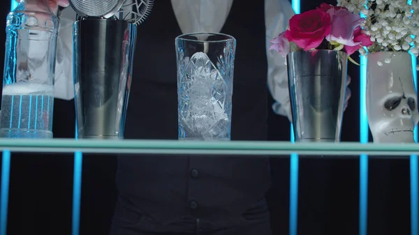 Royal Long Island Cocktail yapımı. Barmenlerin elleri kristal bardağa buz döküyor.