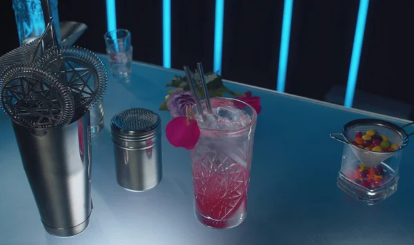 Cherry Sling kokteylini bardaki cam bir masanın üzerinde kristal bardakta kapat. Pembe köpüklü uzun bir içki. Çiçekler, çalkalayıcı ve masada bir kap