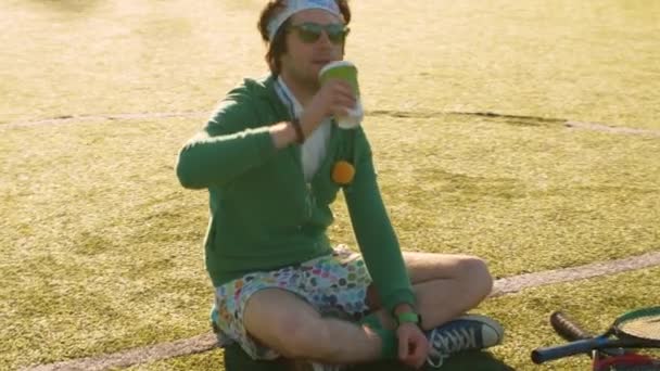 Monstruo divertido sentado en la cancha de tenis y bebiendo té — Vídeo de stock
