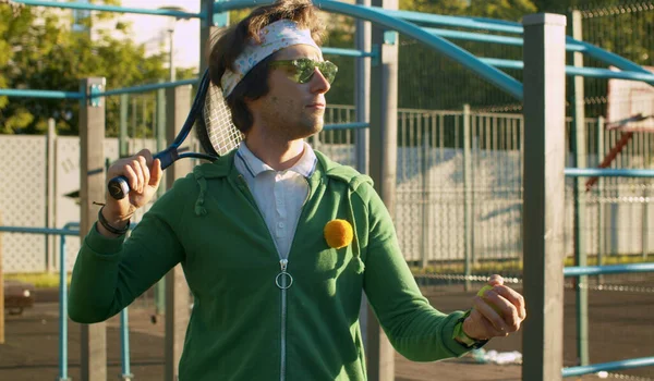 Spor sahasında yeşil güneş gözlüklü, tenis raketli tuhaf adam. Spor mizah anlayışı.