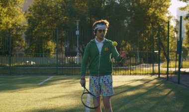 Elinde tenis raketiyle parktaki spor sahasında tenis oynayan tuhaf bir adam. Spor mizah anlayışı.