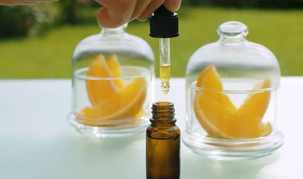 Portakal aromalı yağı damlatan eli kapat. Masanın üzerinde cam kavanozların içindeki turunçgiller. Şifalı bitkiler. Kozmetik, eczane ve aromaterapi için bitkiler. Kamerayla yakın çekim yap veya hareket ettir.