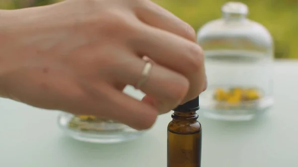 用手滴圣约翰麦芽精油 桌上放着玻璃瓶里的花 治疗草药 天然药物和芳香疗法的概念 用滑梯或移动相机拍摄的闭合镜头 — 图库照片