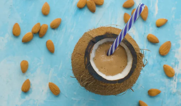 Hindistan cevizli bademli smoothie 'yi kapat. Sağlıklı taze gıda konsepti. Mavi arka planda Almand fındıkları. Üst görünüm