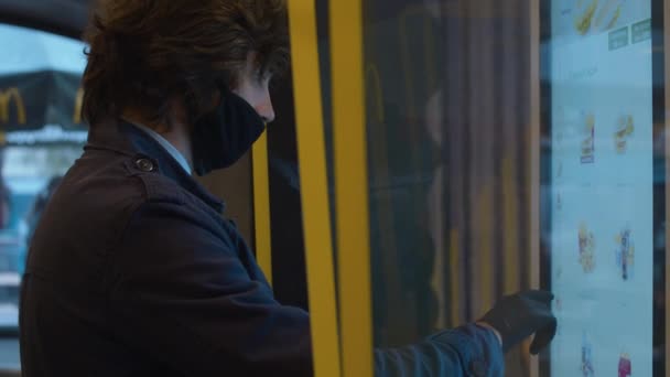 Молодий чоловік в захисній масці вибирає їжу в сенсорному терміналі самообслуговування — стокове відео