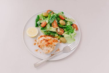 Yeşillikli taze salata, tavuklu kiraz ve zeytin üzerine kırmızı biber serpiştirilmiş, limon dilimi ve beyaz tabakta çatal..